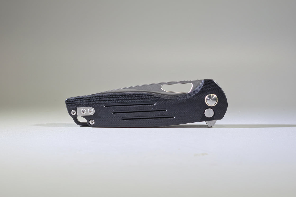Black folding knife on a white surface with a blurred background